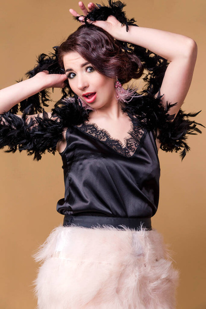 Brunette beautiful woman in boa from ostrich feathers on beige background. Model in shock and amazement. Verycal photo - Foto, immagini