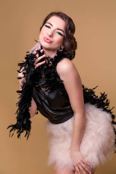 Brunette beautiful woman in boa from ostrich feathers is  fooling around and grimacing on a beige background. Vertycal photo - Foto, Imagem