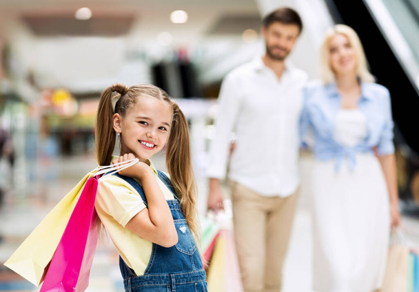 Figlia Holding borse a piedi con i genitori tra negozi nel centro commerciale - Foto, immagini