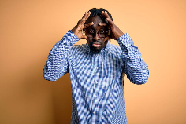 Young handsome african american man wearing shirt and glasses over yellow background Trying to open eyes with fingers, sleepy and tired for morning fatigue - Foto, Bild