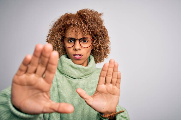 Joven mujer afroamericana hermosa con jersey de cuello alto y gafas haciendo gesto de stop con palmas de las manos, expresión de enojo y frustración
 - Foto, Imagen