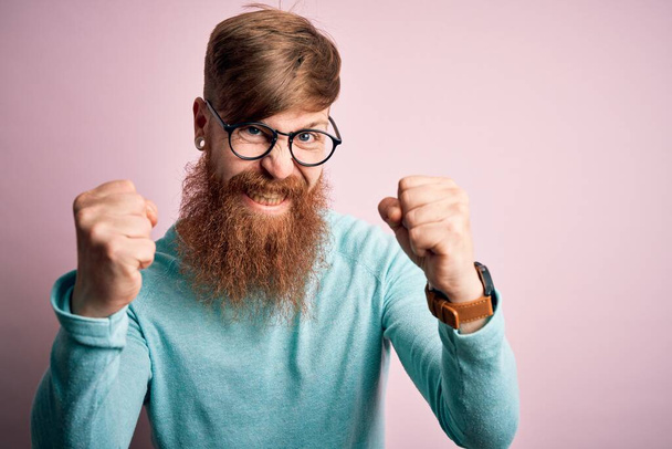 Handsome Irish redhead man with beard wearing glasses over pink isolated background angry and mad raising fists frustrated and furious while shouting with anger. Rage and aggressive concept. - Photo, Image