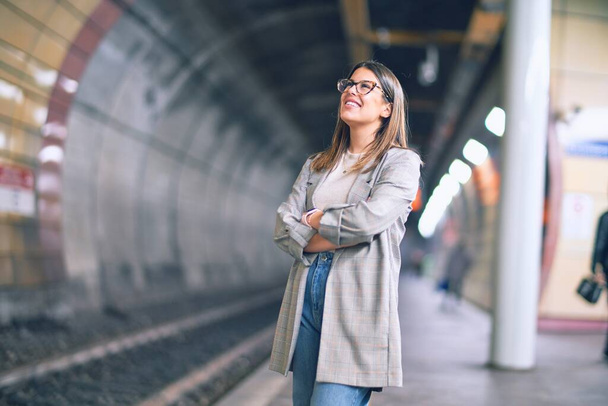 Молодая красивая женщина улыбается счастливой и уверенной. Стоя с улыбкой на лице на платформе железнодорожного вокзала
 - Фото, изображение
