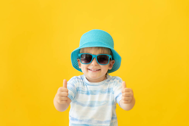 Portrait of happy child showing thumbs up against yellow background. Kid having fun on summer vacation. Dream and imagination concept - Fotoğraf, Görsel