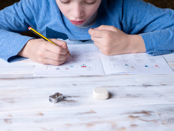 7-летний мальчик сидел за столом и делал домашнюю работу.
 - Фото, изображение