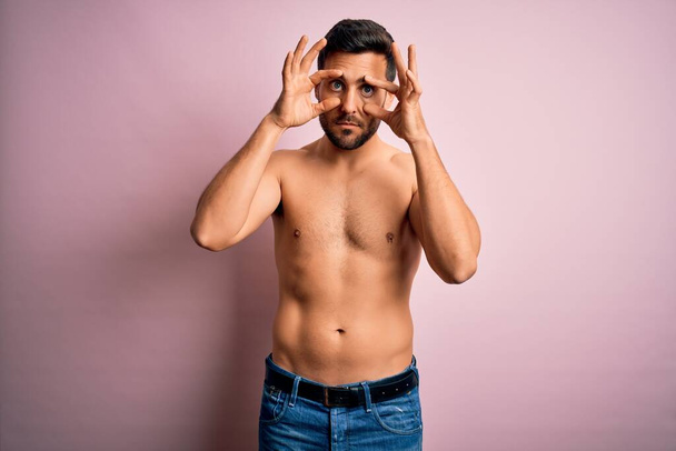 Νέος όμορφος δυνατός άντρας με γενειάδα χωρίς πουκάμισο στέκεται πάνω από απομονωμένο ροζ φόντο προσπαθώντας να ανοίξει τα μάτια με τα δάχτυλα, νυσταγμένος και κουρασμένος για την πρωινή κούραση - Φωτογραφία, εικόνα
