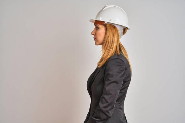 Redhead caucasian business woman wearing safety helmet over isolated background looking to side, relax profile pose with natural face with confident smile. - Foto, immagini
