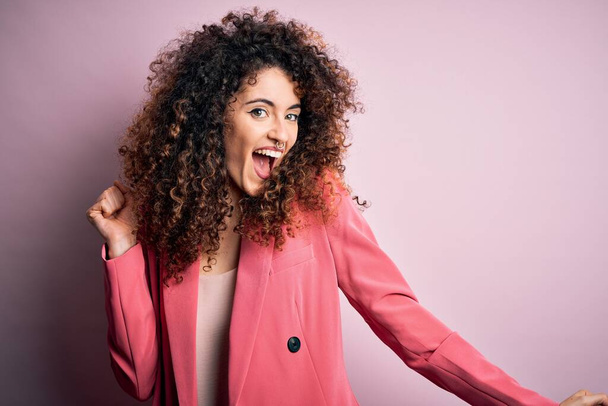 Young beautiful businesswoman with curly hair and piercing wearing elegant jacket Dancing happy and cheerful, smiling moving casual and confident listening to music - Photo, Image