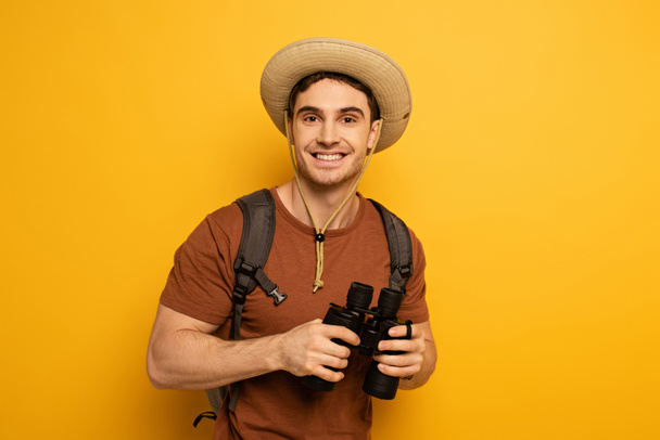 jóképű boldog utazó kalap hátizsák gazdaság távcső sárga - Fotó, kép
