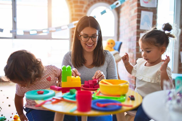 Jeune belle enseignante et tout-petits jouant sur la table avec beaucoup de jouets à la maternelle
 - Photo, image