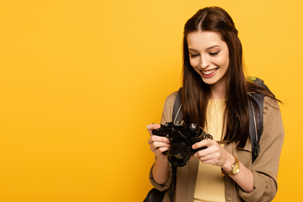 attractive happy female tourist with backpack holding photo camera on yellow  - Photo, Image