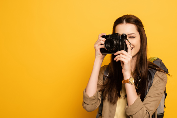 attractive female tourist with backpack holding photo camera on yellow  - Photo, Image