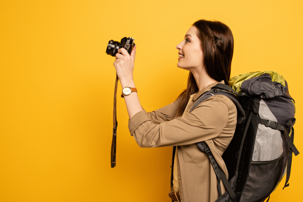 turista animado com mochila segurando câmera de fotos no amarelo
 - Foto, Imagem