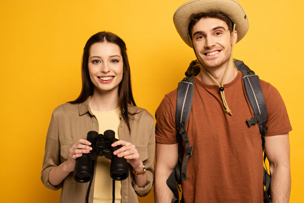 casal de viajantes felizes com mochila e binóculos, isolado em amarelo
 - Foto, Imagem