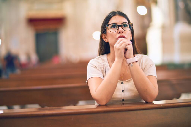 Fiatal, gyönyörű nő térden állva imádkozik egy padon a templomban - Fotó, kép