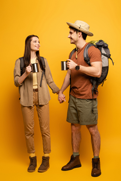 couple of happy tourists with backpacks and cups of coffee holding hands on yellow - Foto, immagini