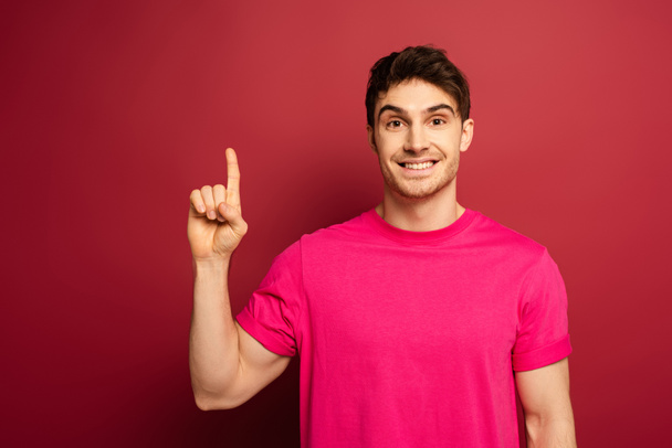 portrait of smiling man in pink t-shirt pointing up on red - Foto, imagen
