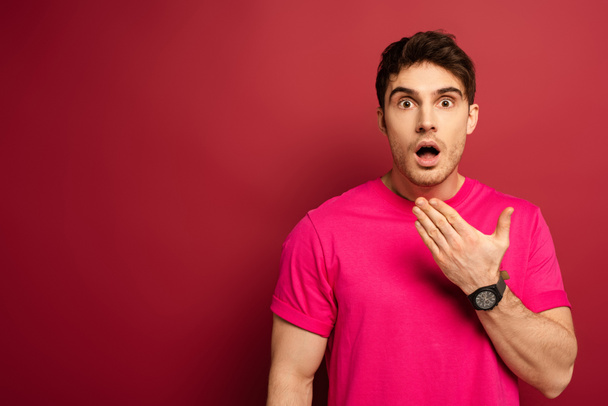 πορτρέτο του έκπληκτου άνδρα με ανοιχτό το στόμα σε ροζ t-shirt σε κόκκινο - Φωτογραφία, εικόνα