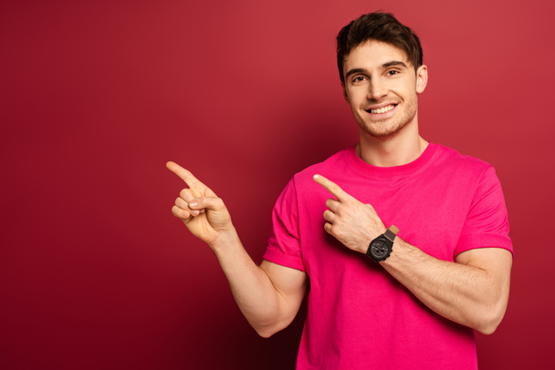 portrait of smiling man in pink t-shirt pointing on red - Foto, Imagen