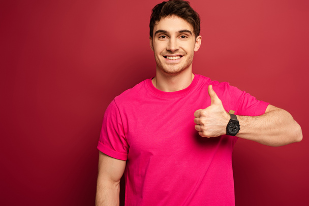 portrait of smiling man in pink t-shirt showing thumb up on red - Foto, immagini