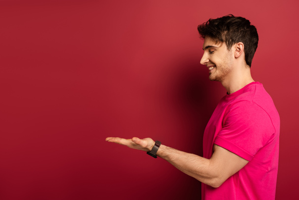 portrait of smiling man in pink t-shirt presenting something on red - Foto, Imagem