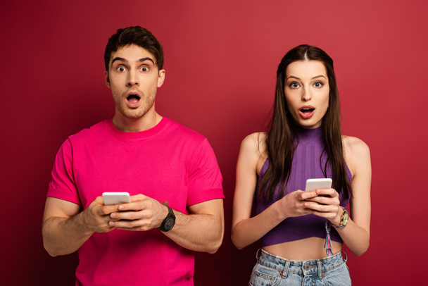 beautiful shocked couple using smartphones on red - Фото, зображення