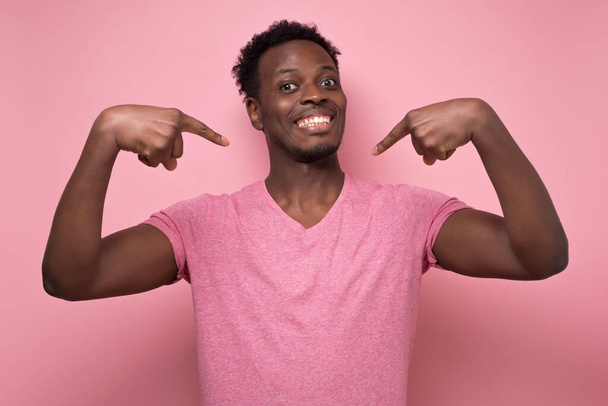Joven africano positivo sonriendo y señalándose a sí mismo con los dedos índice
. - Foto, imagen