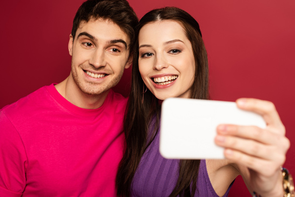 beautiful cheerful couple taking selfie on smartphone on red - Foto, Imagen