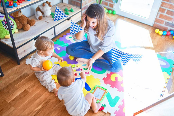 Hermosa maestra y niños pequeños jugando alrededor de un montón de juguetes en el jardín de infantes
 - Foto, imagen