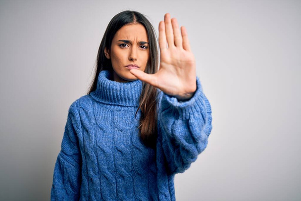 Young beautiful brunette woman wearing casual turtleneck sweater over white background doing stop sing with palm of the hand. Warning expression with negative and serious gesture on the face. - Photo, Image