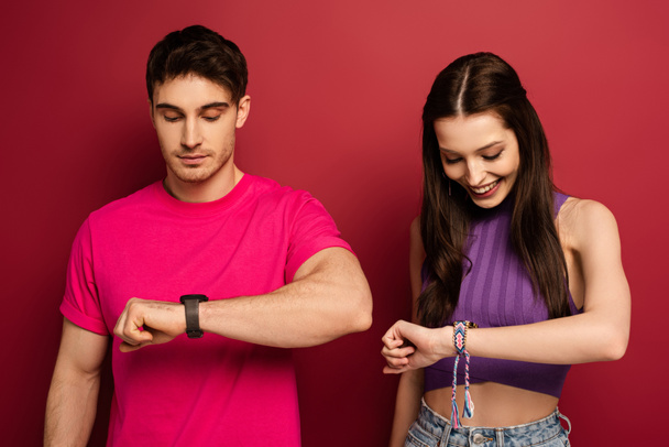 happy couple looking at wristwatches on red - Valokuva, kuva