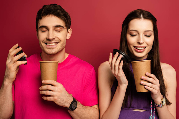 beautiful happy couple smelling coffee in disposable cups on red - Foto, afbeelding