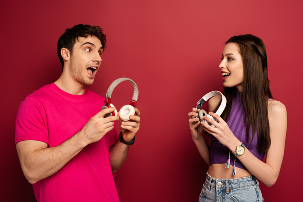 beautiful excited couple holding headphones on red - Foto, imagen
