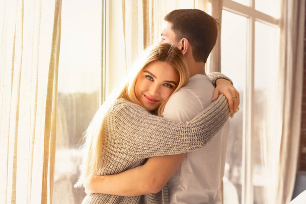 Young guy and girl hugging near window in sunlit room - Photo, Image