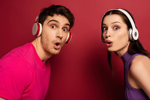 beautiful surprised couple listening music with headphones on red - Foto, Imagem