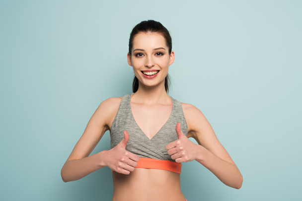 beautiful happy athletic woman standing in sportswear and showing thumbs up on blue - Photo, Image