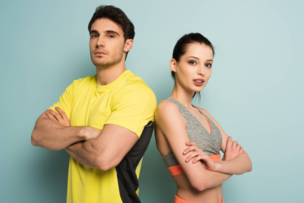 sebevědomý atletický pár stojící ve sportovním oblečení se zkříženýma rukama na modré - Fotografie, Obrázek