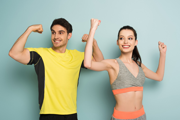 χαρούμενο αθλητικό ζευγάρι στέκεται σε αθλητικά ενδύματα που δείχνουν μυς στο μπλε - Φωτογραφία, εικόνα