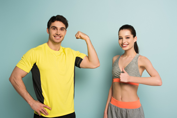 happy sportsman showing muscles while girl showing thumbs up on blue - Фото, изображение