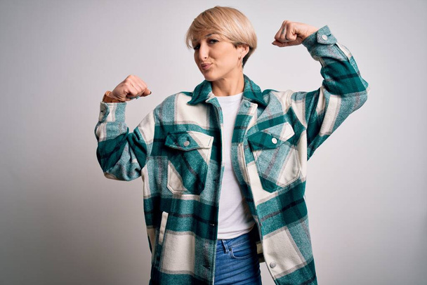 Young blonde woman with short hair wearing casual retro green shirt over isolated background showing arms muscles smiling proud. Fitness concept. - Photo, Image