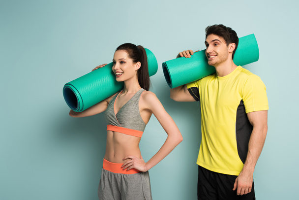 smiling sportive couple holding fitness mats on blue - Фото, изображение