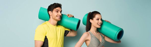 panoramic shot of smiling athletic couple holding fitness mats on blue - Fotó, kép