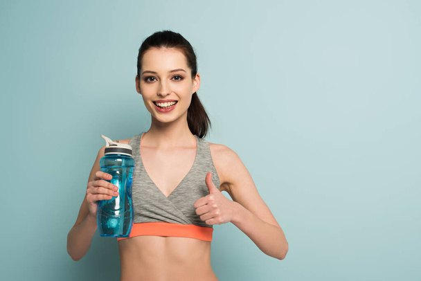 boldog sportos nő kezében sport palack vízzel, és mutatja hüvelykujját fel a kék - Fotó, kép