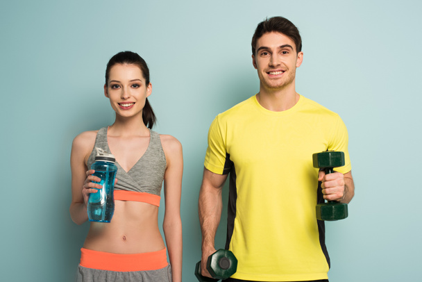 beautiful athletic couple holding dumbbells and sports bottle of water on blue - Fotografie, Obrázek
