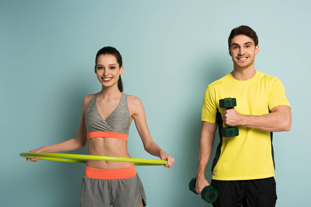 cheerful athletic couple training with dumbbells and hula hoop on blue - Foto, Bild