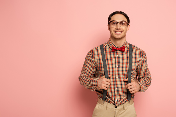 Lächelnder männlicher Nerd mit Brille und Hosenträgern auf rosa - Foto, Bild