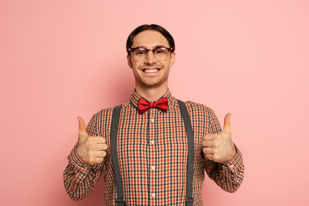 cheerful male nerd in eyeglasses showing thumbs up on pink - Photo, image