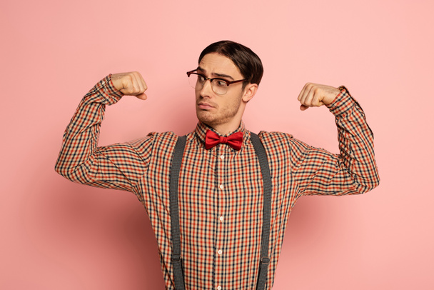 přemýšlivý mužský nerd v brýlích ukazující svaly na růžové - Fotografie, Obrázek