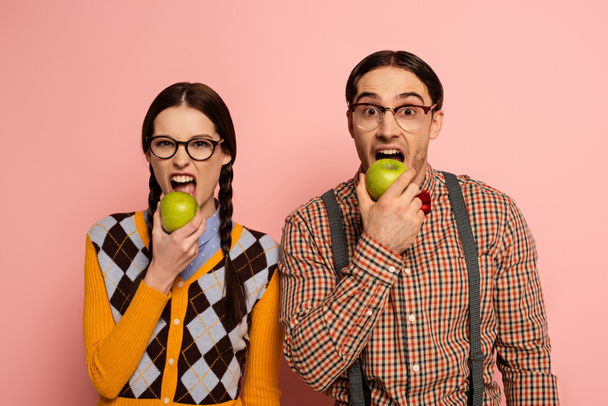couple of nerds in eyeglasses eating apples on pink - Photo, Image