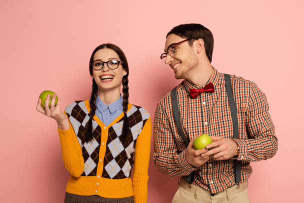couple of happy nerds in eyeglasses holding apples on pink - Foto, afbeelding